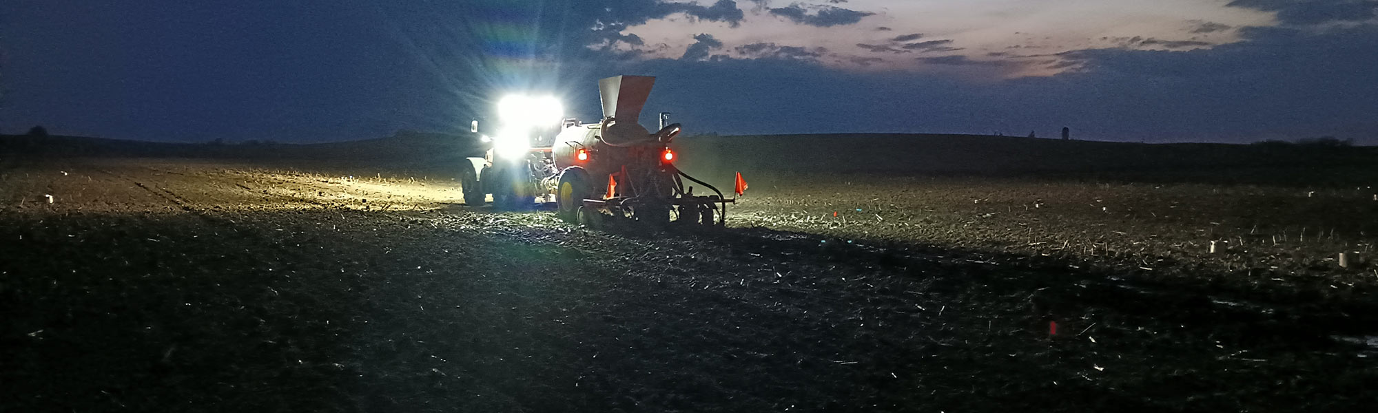 Tractor pulling manure spreader at night